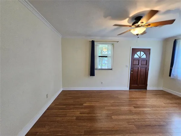a view of an empty room with wooden floor and a ceiling fan