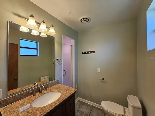 a bathroom with a granite countertop sink vanity mirror and toilet