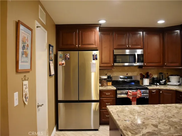 a kitchen with stainless steel appliances granite countertop a refrigerator stove a sink dishwasher and wooden cabinets with wooden floor