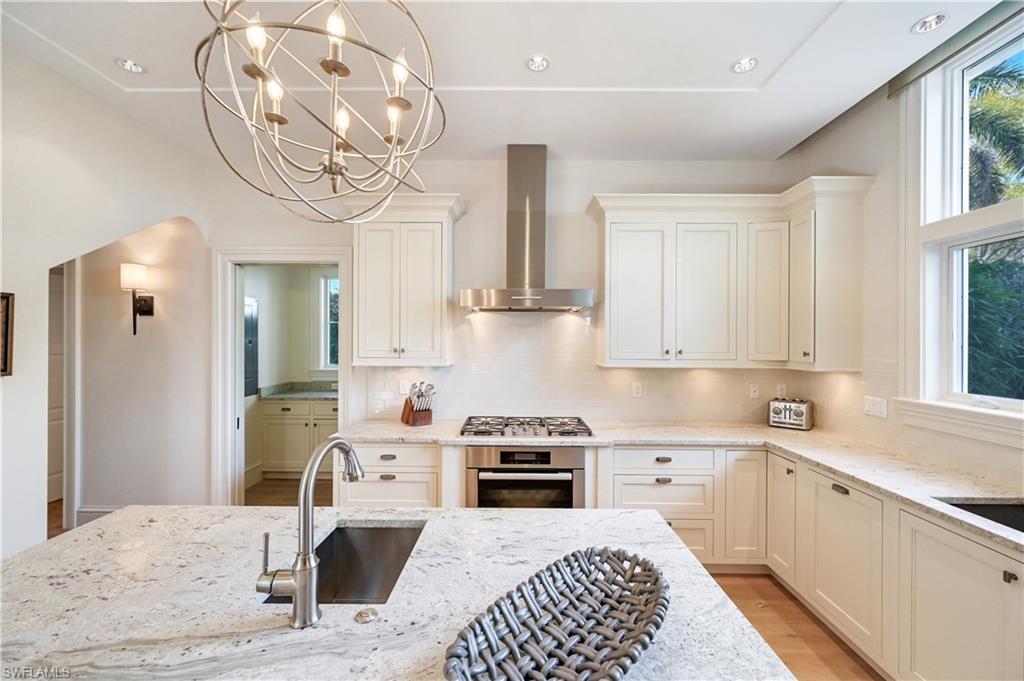 42 6th Street South Naples, FL 34102 - Photo 23 of 46 Kitchen featuring light stone countertops, stainless steel appliances, hanging lights, light wood-style flooring, and decorative backsplash
