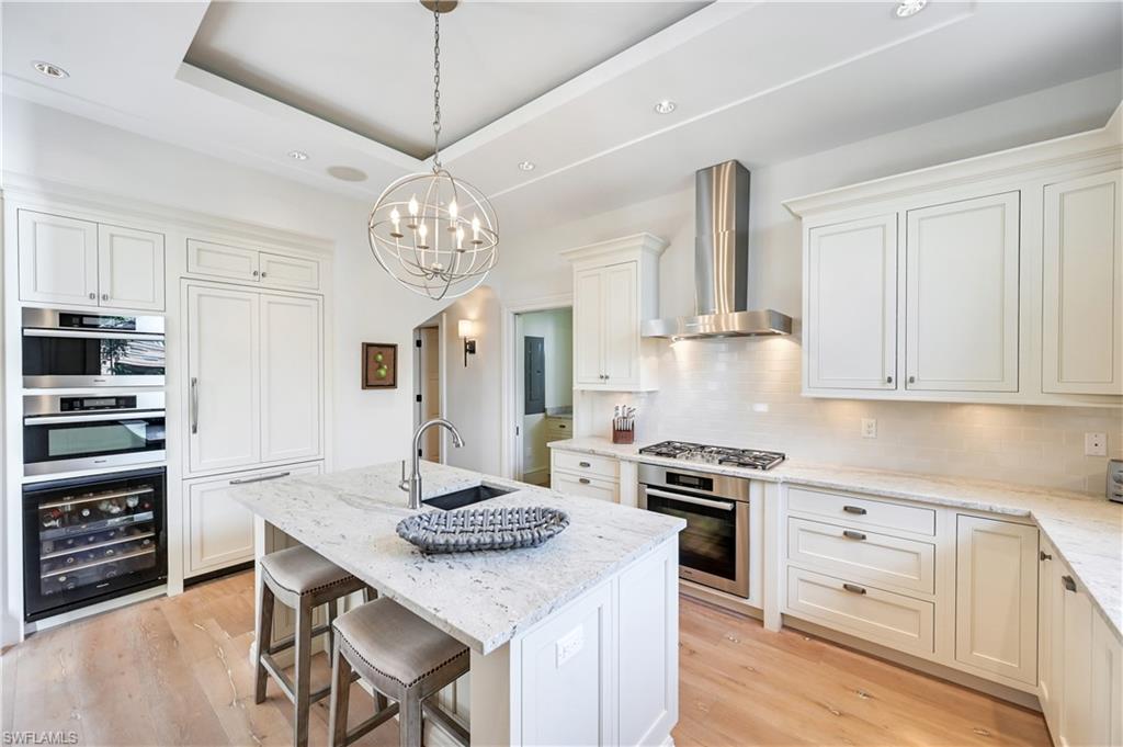 42 6th Street South Naples, FL 34102 - Photo 24 of 46 Kitchen with a breakfast bar, light stone countertops, a kitchen island with sink, beverage cooler, and a tray ceiling