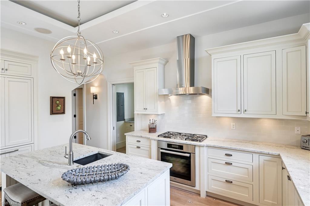 42 6th Street South Naples, FL 34102 - Photo 25 of 46 Kitchen with light stone countertops, stainless steel appliances, white cabinetry, an island with sink, and backsplash