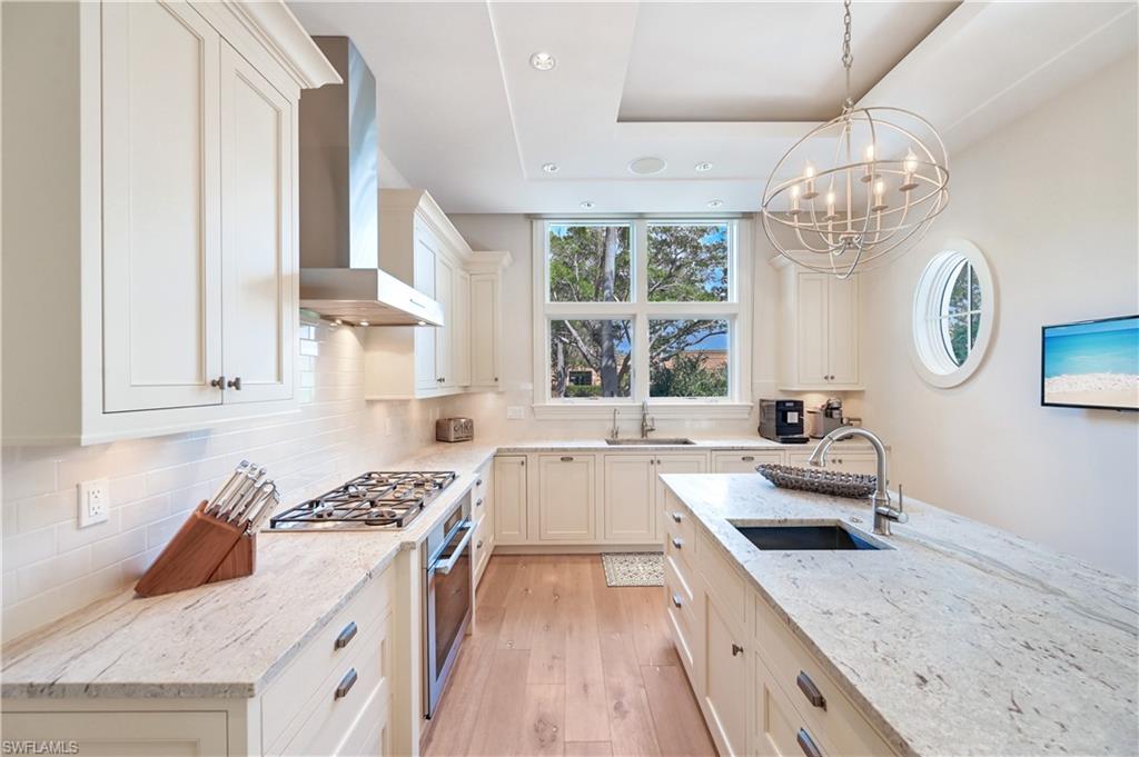 42 6th Street South Naples, FL 34102 - Photo 26 of 46 Kitchen with light stone countertops, light wood-style floors, stainless steel appliances, suspended lighting, and decorative backsplash