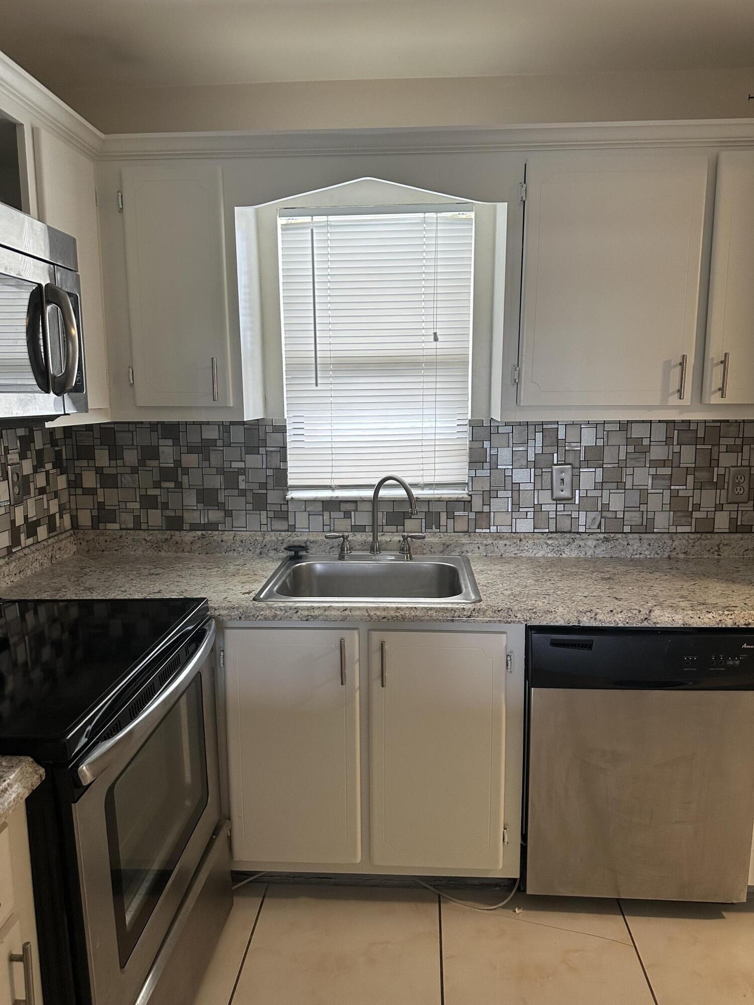 9355 Southwest 8th Street, Unit 311 Boca Raton, FL 33428 - Photo 4 of 17 a kitchen with granite countertop a sink stove and cabinets