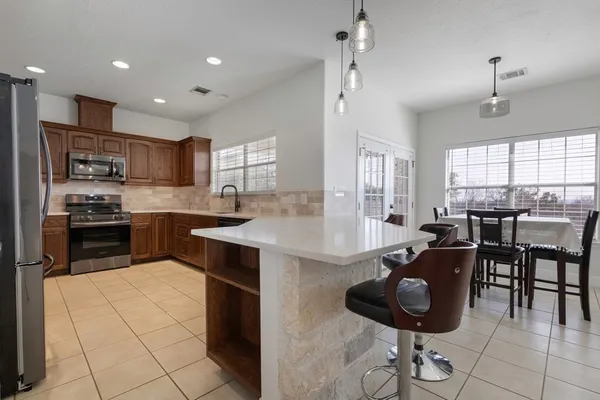 a kitchen with stainless steel appliances kitchen island granite countertop a refrigerator a stove a sink a dining table and chairs with wooden floor