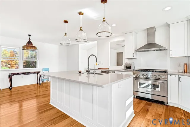 a living room with stainless steel appliances kitchen island granite countertop a stove a sink dishwasher and white cabinets with wooden floor