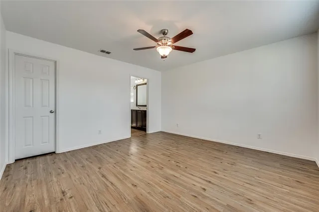 a view of an empty room with wooden floor and a ceiling fan