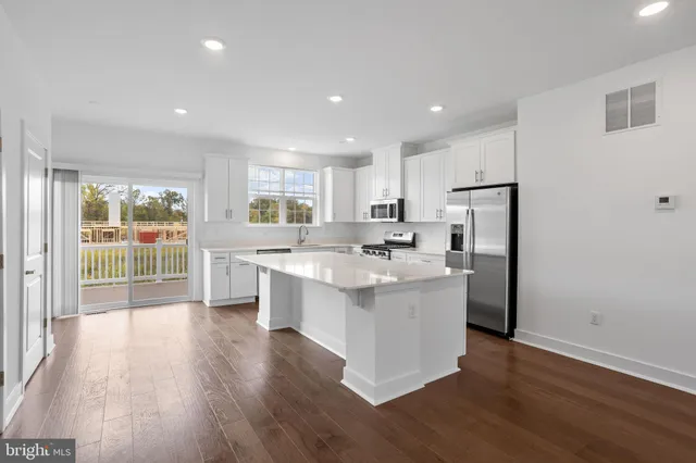 a kitchen with stainless steel appliances granite countertop a refrigerator a sink a stove and white cabinets with wooden floor