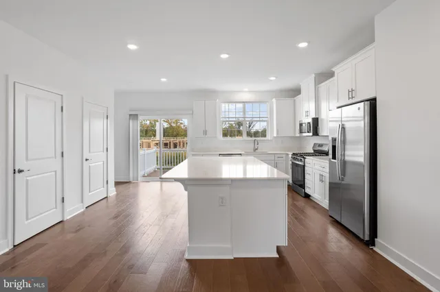 a kitchen with stainless steel appliances granite countertop a refrigerator a sink dishwasher a stove and white countertops with wooden floor