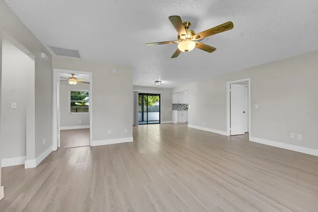 a view of an empty room with wooden floor and a ceiling fan