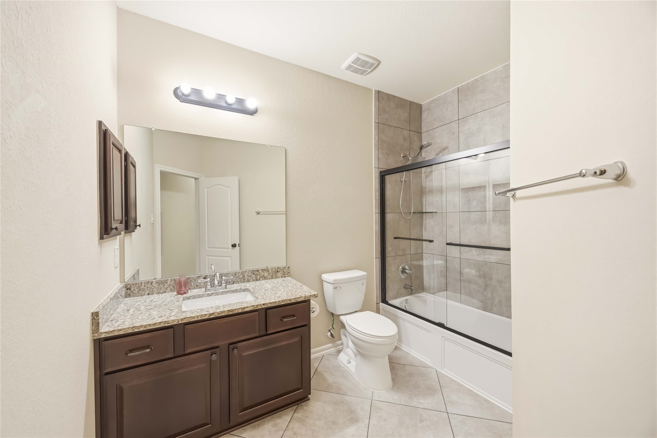 17206 Upper Ridge Lane Humble, TX 77346 - Photo 24 of 33 Secondary Bathroom – Stylish full bath featuring granite counters, dark wood cabinetry, and a tiled tub/shower combo with glass enclosure.