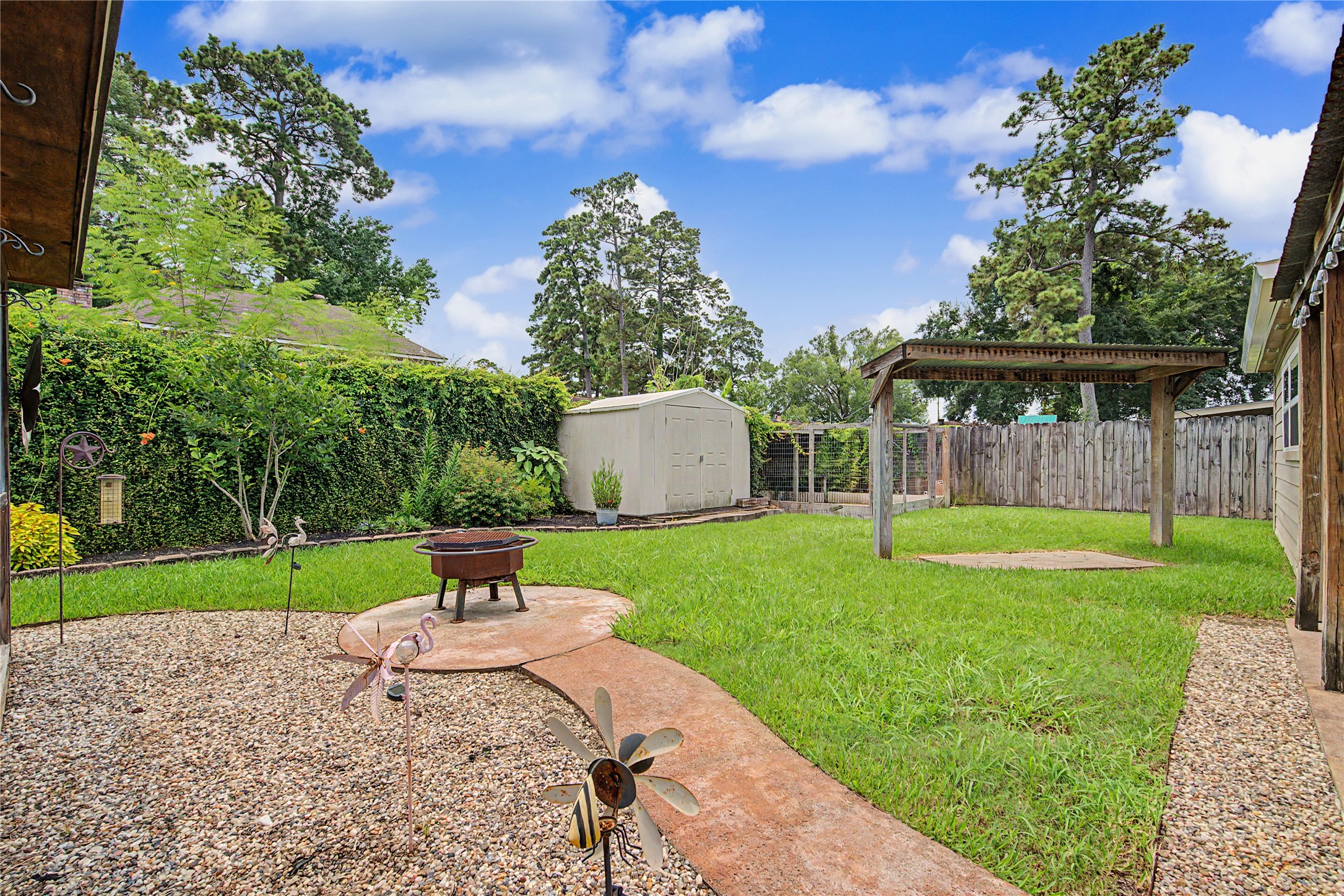 4210 Mossygate Drive Spring, TX 77373 - Photo 29 of 33 This backyard features a spacious grassy area with a fire pit/grill, a charming pergola, and a large storage shed. The space is bordered by a wooden privacy fence and lush greenery, offering a peaceful outdoor retreat.