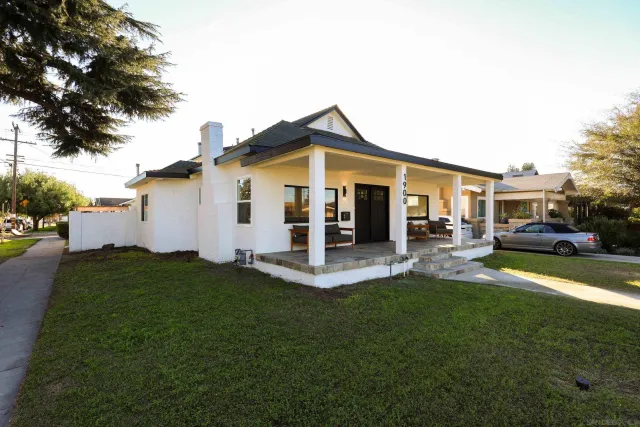 a view of a white house in front of a yard with many windows