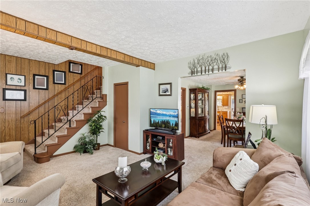 10818 Dixon Road Cleveland, OH 44111 - Photo 8 of 44 Living room featuring a textured ceiling, wooden walls, stairway, carpet flooring, and ceiling fan