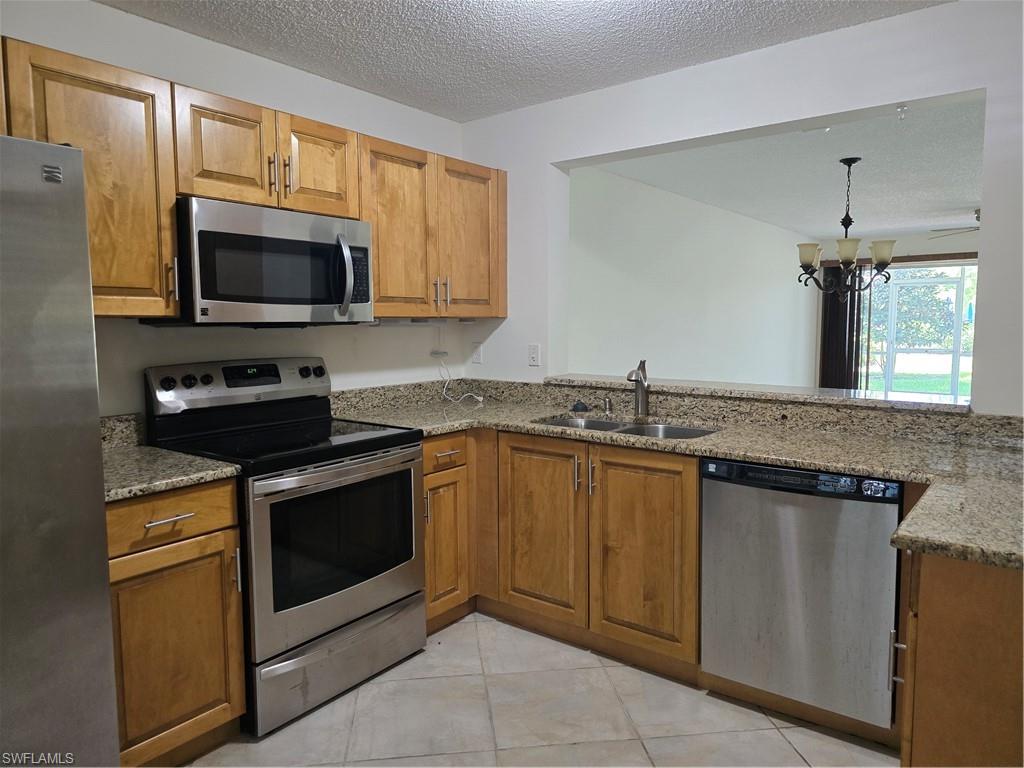 5737 Whitaker Road, Unit C104 Naples, FL 34112 - Photo 19 of 35 Kitchen featuring wood cabinetry, light-toned countertops, stainless steel appliances, and a pass-through opening