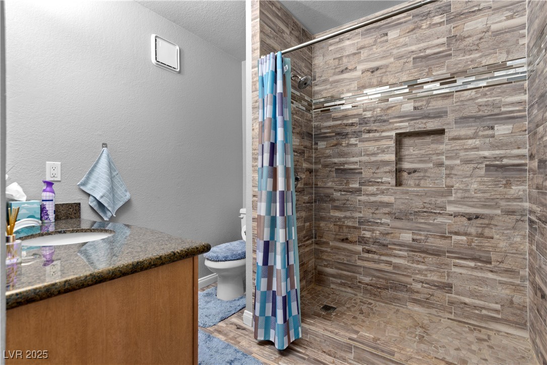 9325 West Desert Inn Road, Unit 141 Las Vegas, NV 89117 - Photo 9 of 30 Bathroom with vanity, a textured wall, tiled shower, a textured ceiling, and light wood finished floors
