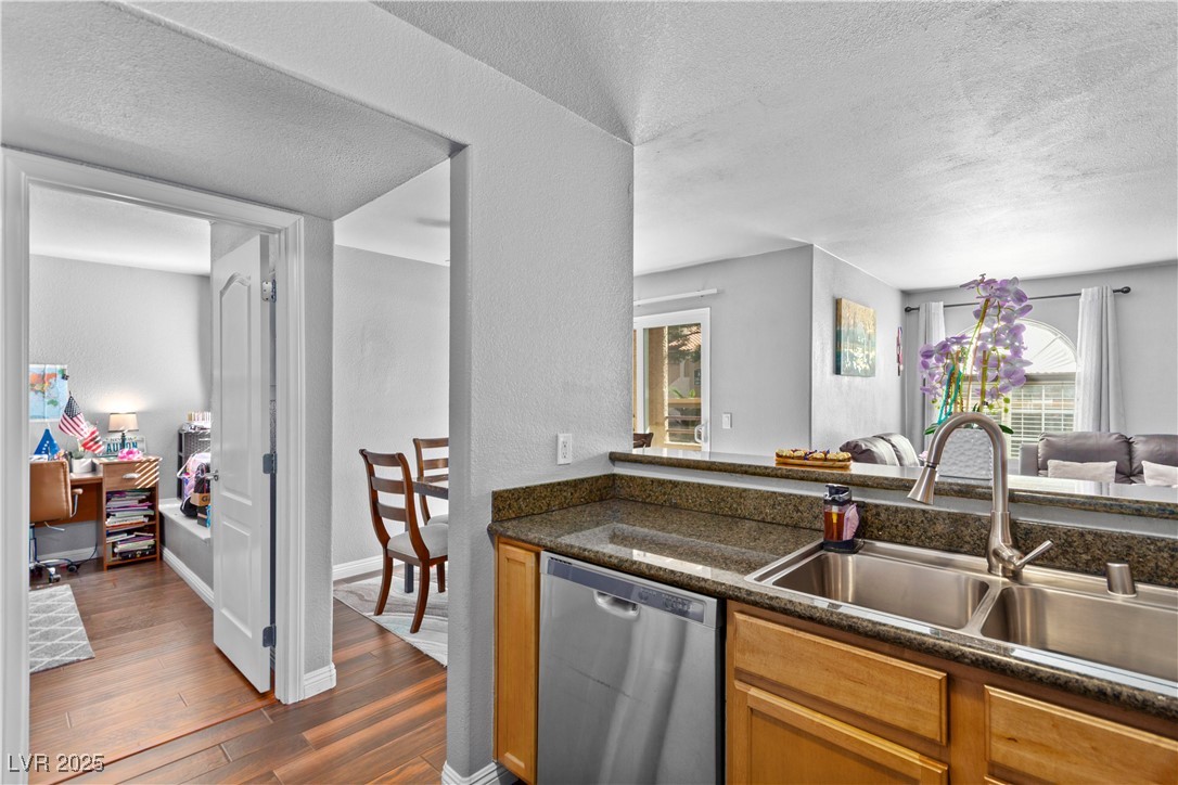 9325 West Desert Inn Road, Unit 141 Las Vegas, NV 89117 - Photo 30 of 30 Kitchen with a textured ceiling, stainless steel dishwasher, open floor plan, dark wood-type flooring, and dark stone counters
