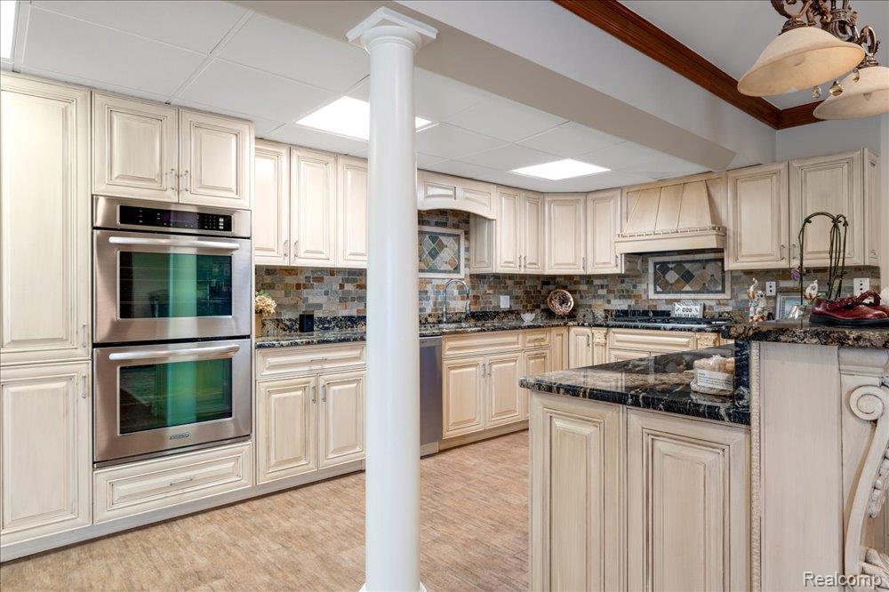 3543 Cedar Brook Drive Rochester, MI 48309 - Photo 51 of 99 Gourmet kitchen featuring double wall ovens, extensive cream cabinetry, dark stone countertops, mosaic tile backsplash, and wood-finish flooring