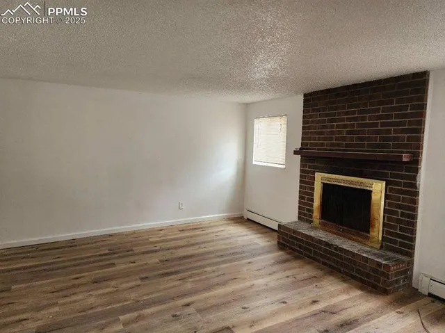 a view of an empty room with wooden floor fireplace and a window