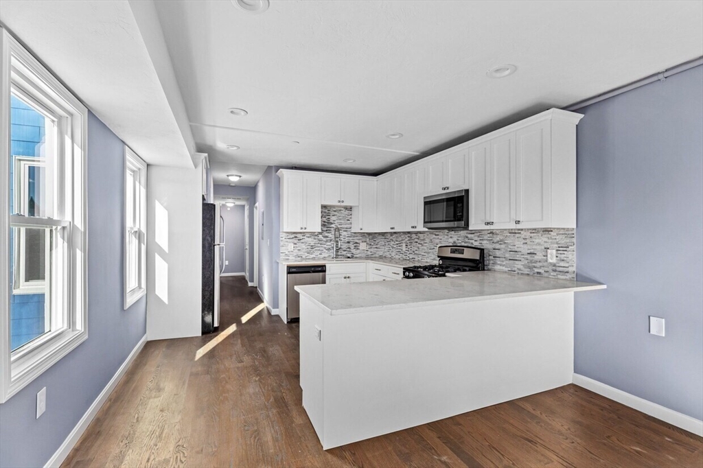 167 Lexington Street, Unit 167 Boston, MA 02128 - Photo 28 of 34 a kitchen with stainless steel appliances a stove top oven a refrigerator a sink dishwasher and a fireplace with wooden floor