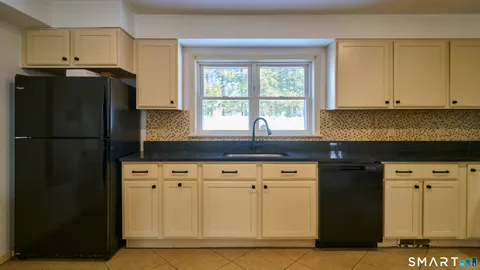 a kitchen with granite countertop a refrigerator a sink and white cabinets