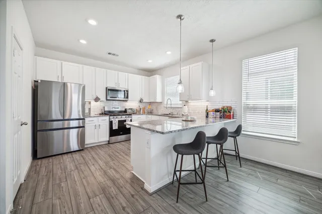 a kitchen with stainless steel appliances granite countertop a refrigerator a sink dishwasher a stove and white countertops with wooden floor