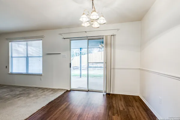 an empty room with wooden floor chandelier and windows