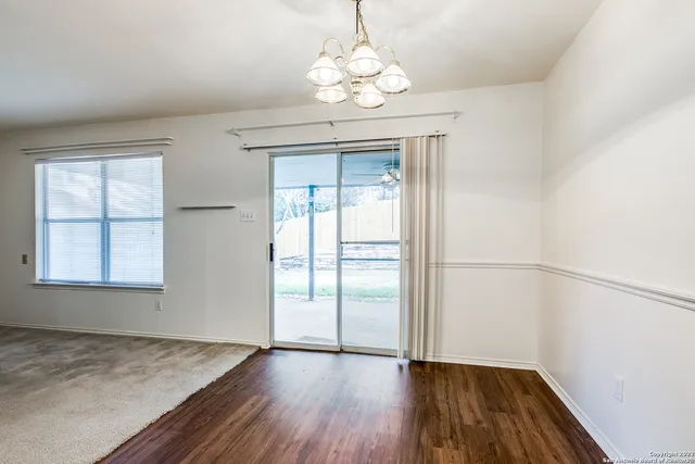 an empty room with wooden floor chandelier and windows
