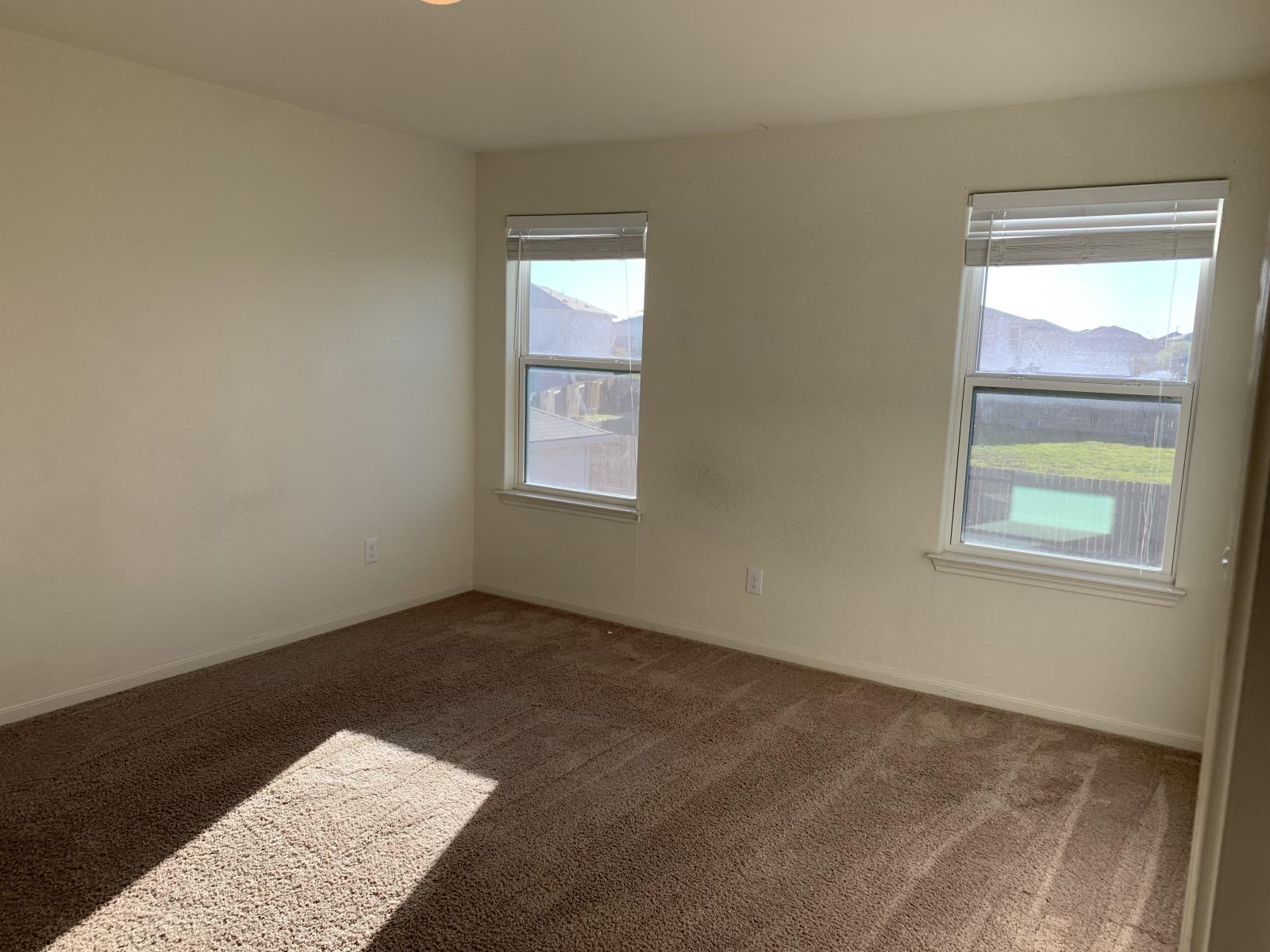 217 Denson Lane Jarrell, TX 76537 - Photo 13 of 26 Interior room featuring two windows with blinds, neutral-toned walls, and brown carpet flooring
