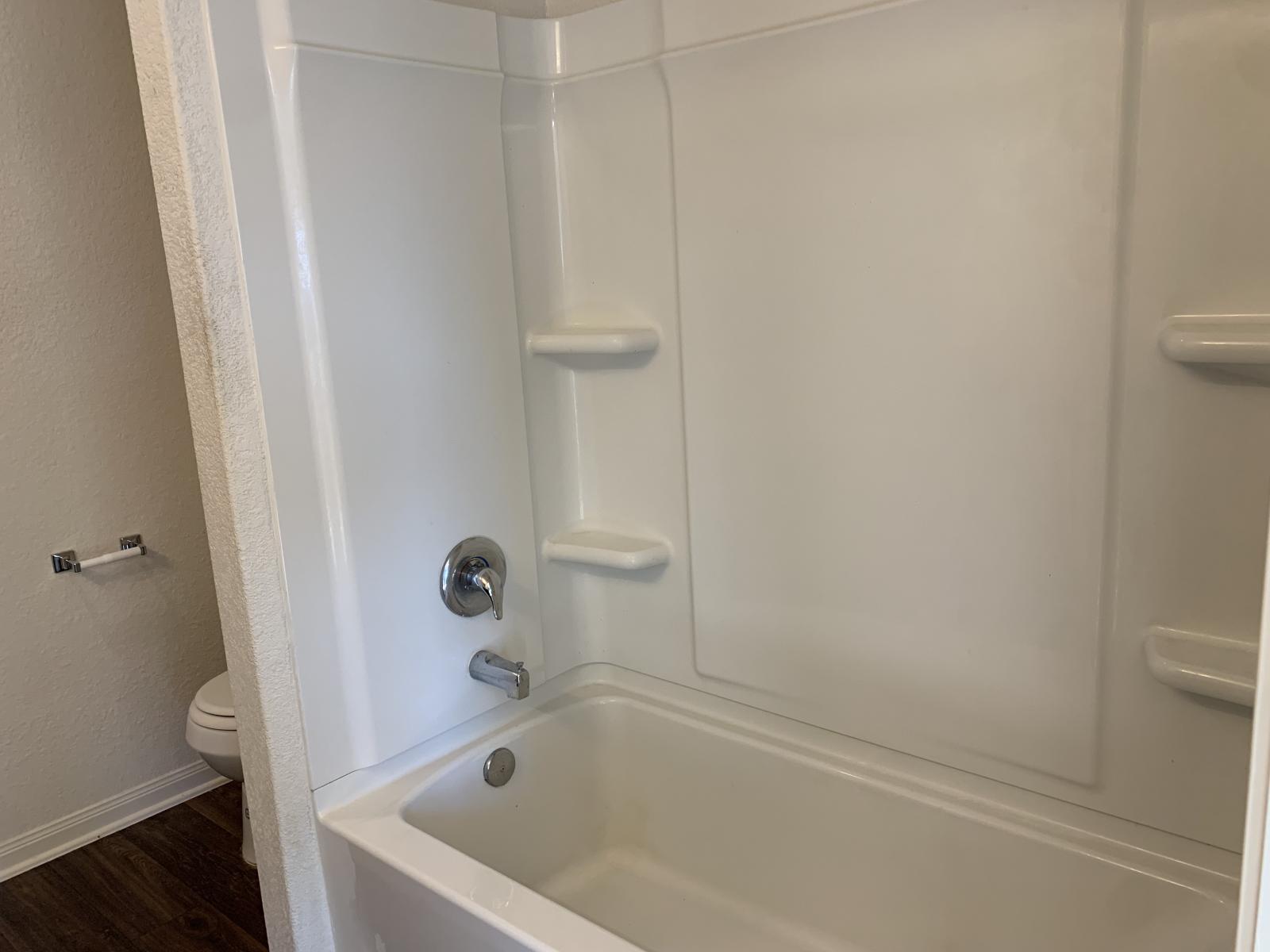 217 Denson Lane Jarrell, TX 76537 - Photo 16 of 26 White fiberglass tub and shower enclosure with integrated shelving, chrome fixtures, and wood-finish flooring