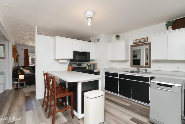 a kitchen with stainless steel appliances a stove top oven a sink dishwasher and a refrigerator with wooden floor