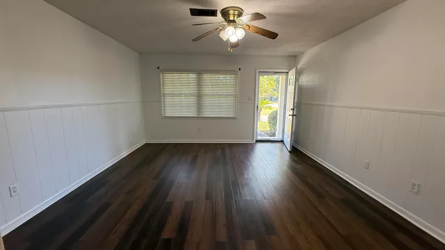 an empty room with wooden floor chandelier fan and windows