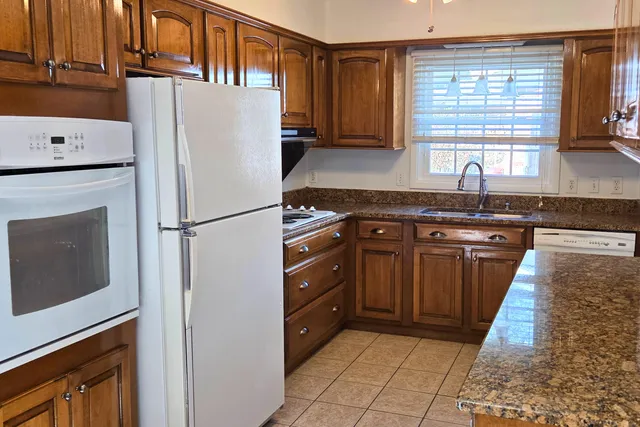a kitchen with granite countertop a refrigerator a sink a stove and wooden cabinets
