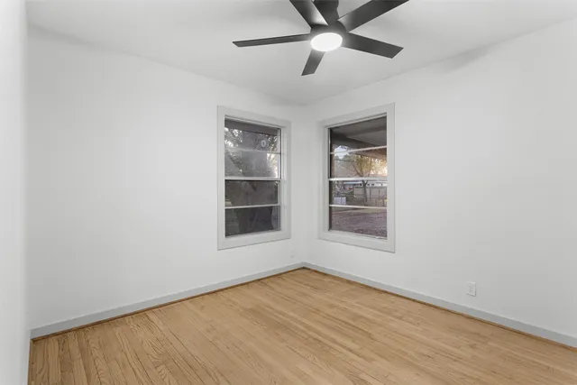 an empty room with wooden floor fan and windows