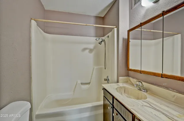 a bathroom with a granite countertop bathtub shower sink vanity and toilet