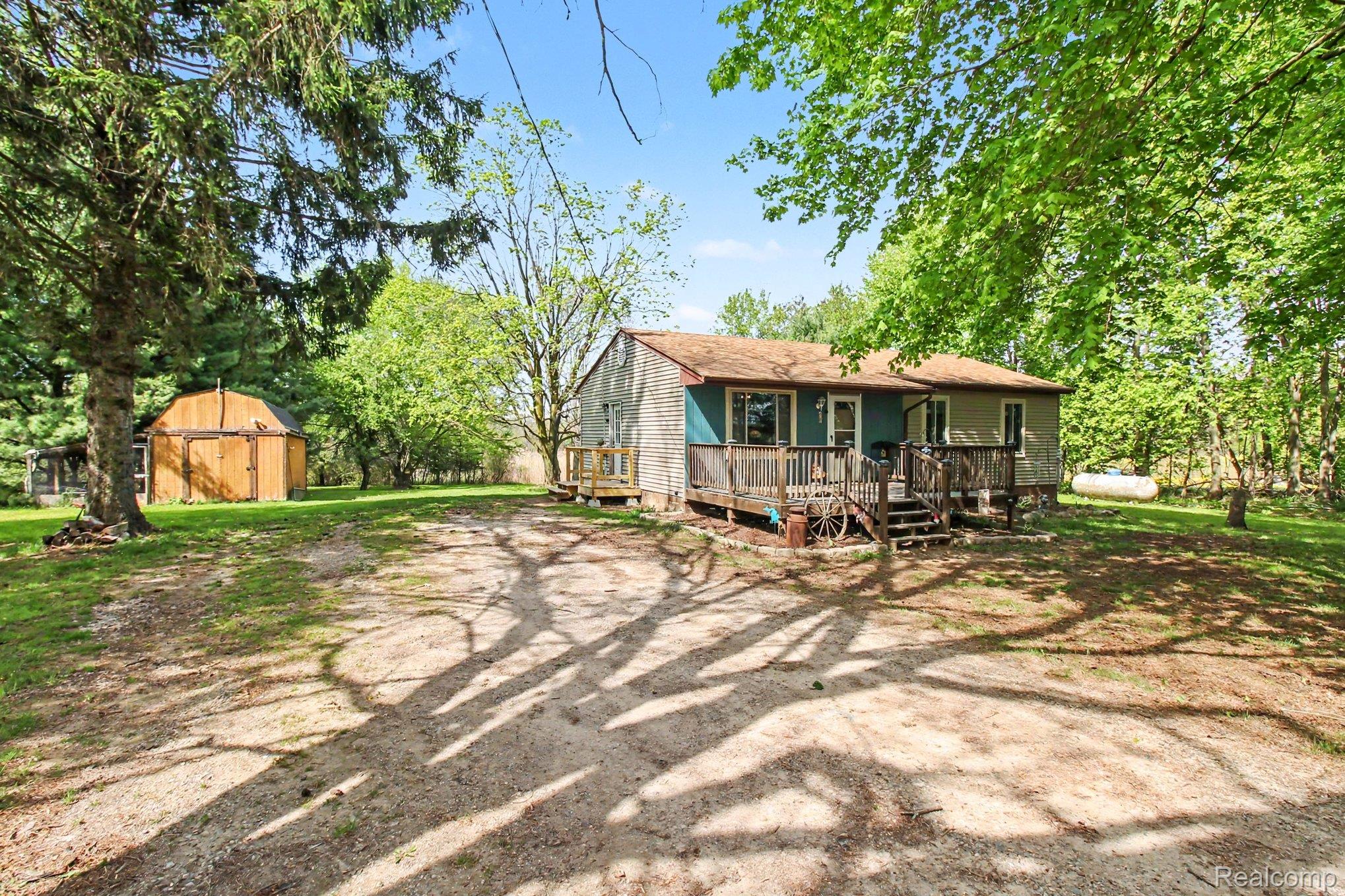 4623 West Lovejoy Road Byron, MI 48418 - Photo 20 of 21 Side view of property featuring a wooden deck, a storage unit, and driveway