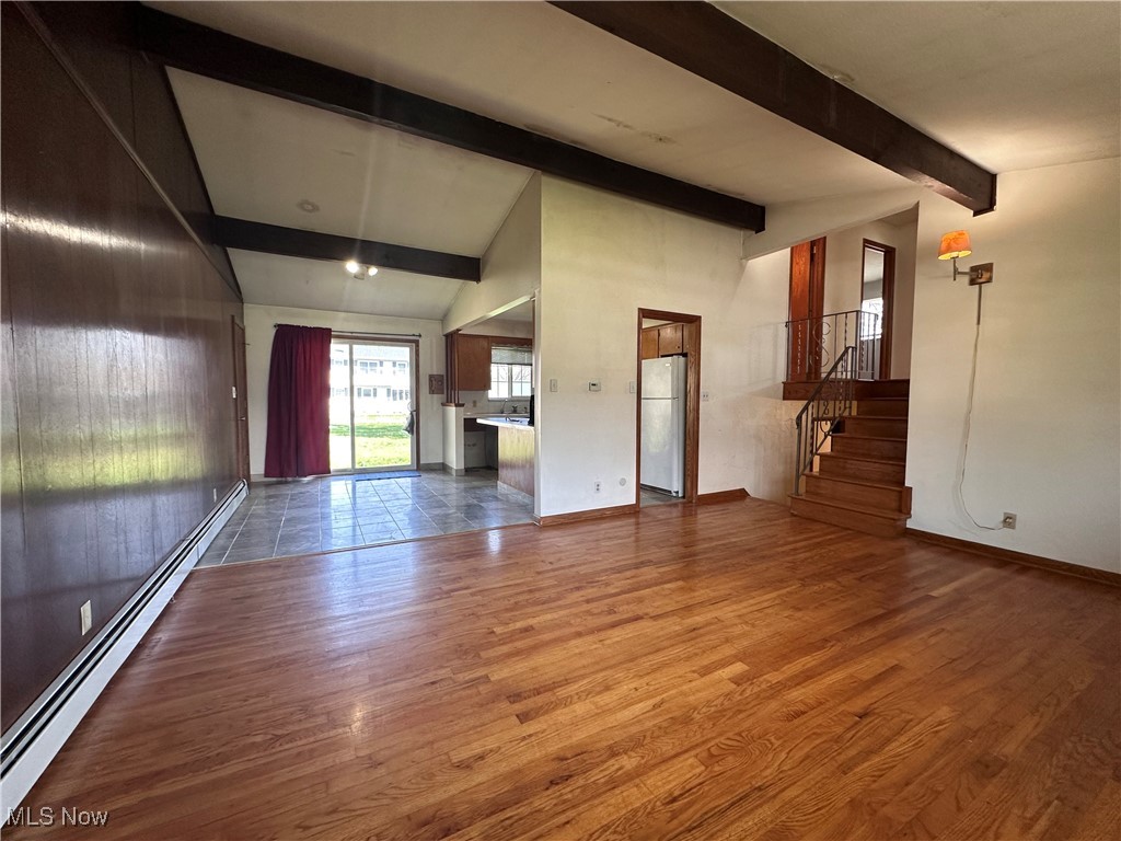 2829 Shellhart Road Barberton, OH 44203 - Photo 5 of 29 Unfurnished living room featuring stairway, lofted ceiling with beams, wood finished floors, and a baseboard radiator