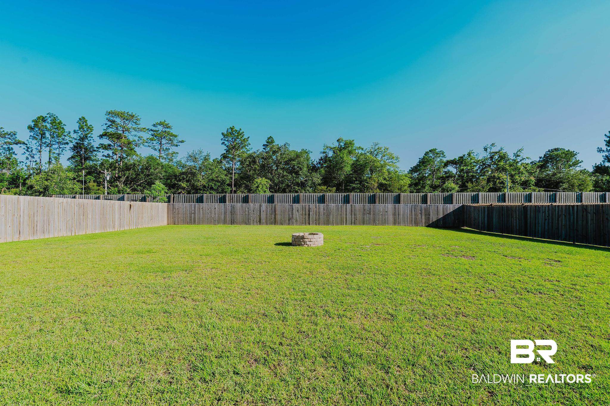 7872 Calverton Street Foley, AL 36535 - Photo 56 of 76 Expansive backyard featuring a lush green lawn, full privacy fencing, and a built-in stone fire pit