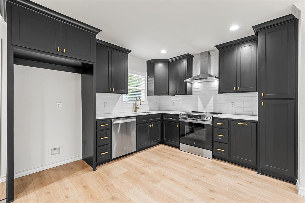 611 North Rita Street Lacy-Lakeview, TX 76705 - Photo 5 of 17 Kitchen with appliances with stainless steel finishes, dark cabinetry, wall chimney exhaust hood, decorative backsplash, and light wood-style flooring