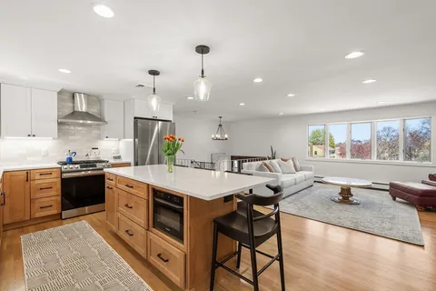 a large kitchen with stainless steel appliances a stove a sink a oven a dining table and chairs with wooden floor