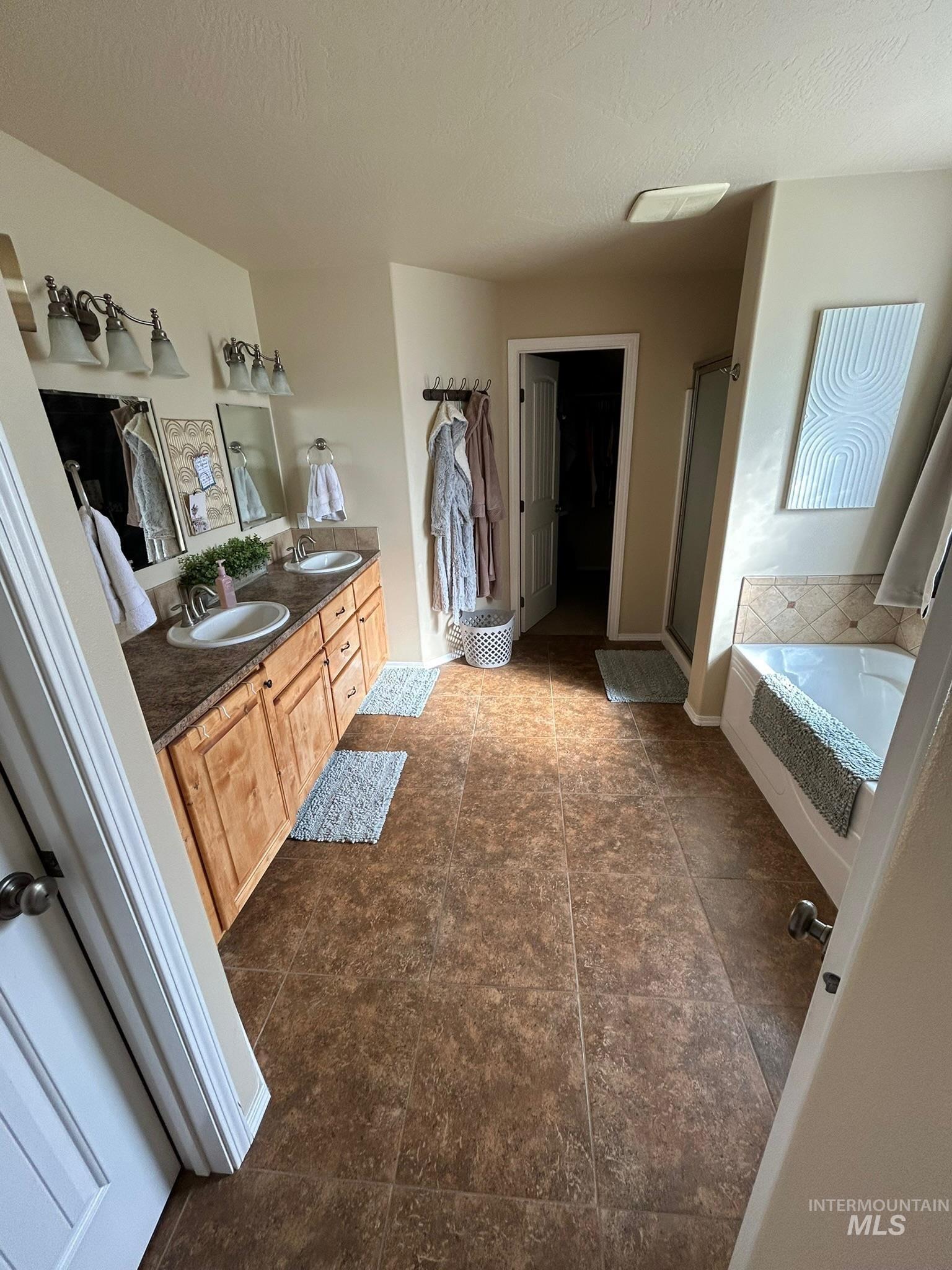 3091 Echo Road Nyssa, OR 97913 - Photo 18 of 36 Full bath with double vanity, a bath, a shower stall, a spacious closet, and dark tile patterned floors