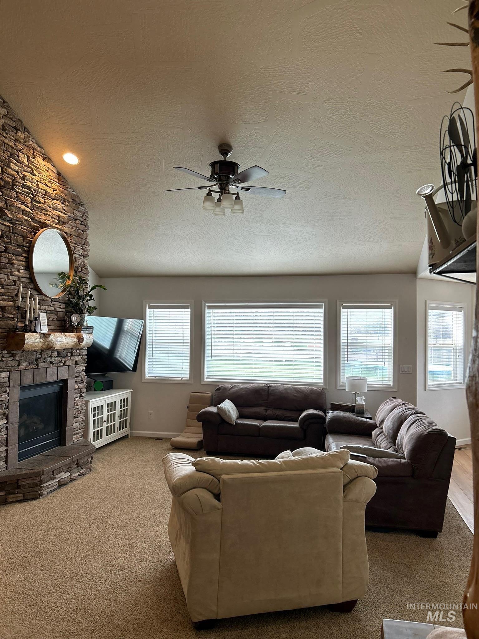 3091 Echo Road Nyssa, OR 97913 - Photo 20 of 36 Living area with a stone fireplace, healthy amount of natural light, lofted ceiling, a ceiling fan, and carpet flooring