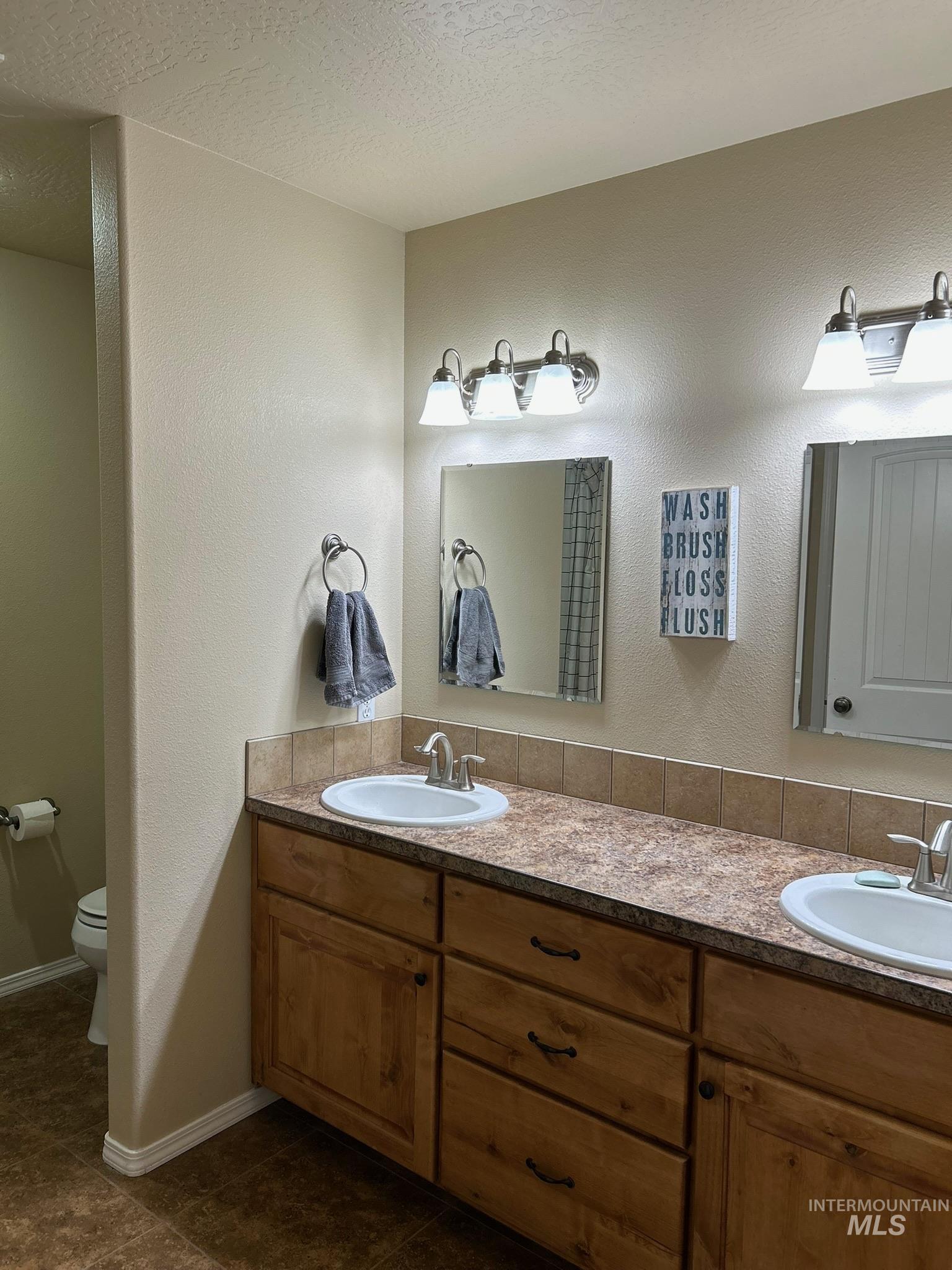 3091 Echo Road Nyssa, OR 97913 - Photo 28 of 36 Bathroom featuring a textured wall, double vanity, a textured ceiling, and dark tile patterned flooring