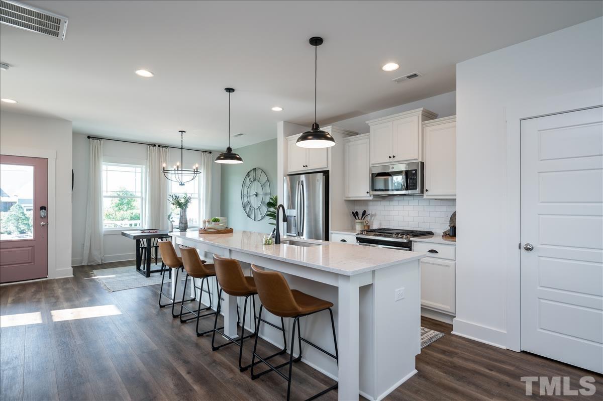 a kitchen with stainless steel appliances granite countertop a stove a refrigerator a kitchen island a dining table and chairs with wooden floor