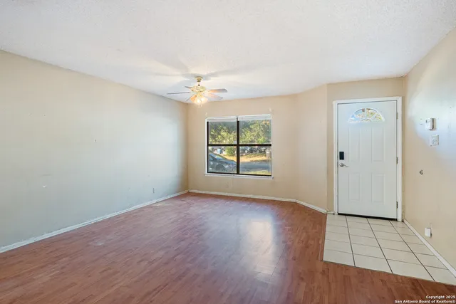 an empty room with wooden floor chandelier fan and windows