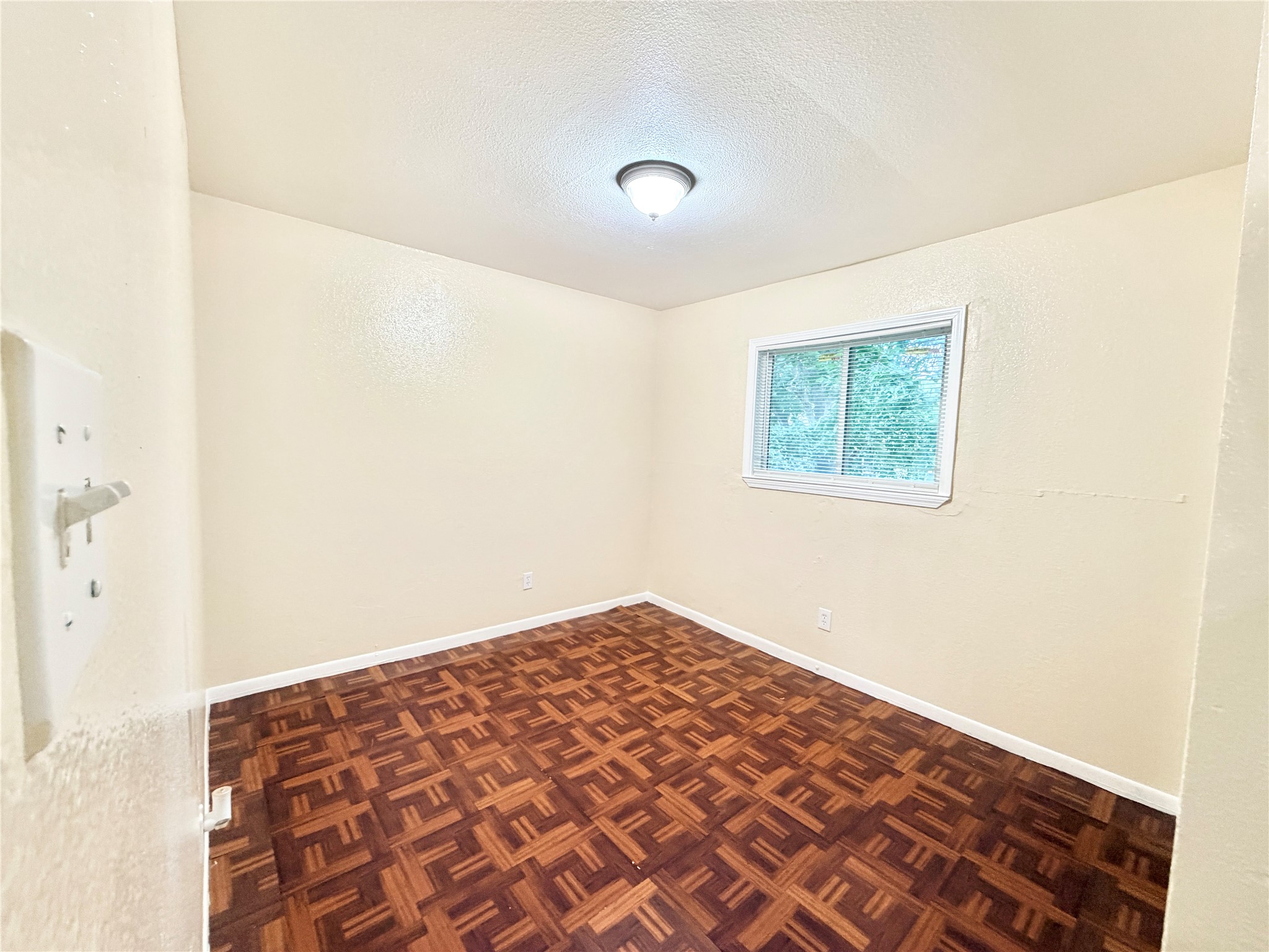6257 Manor Road, Unit B Austin, TX 78723 - Photo 32 of 38 Bright room featuring wood-finish parquet flooring, a single window with white trim, and a ceiling-mounted light fixture