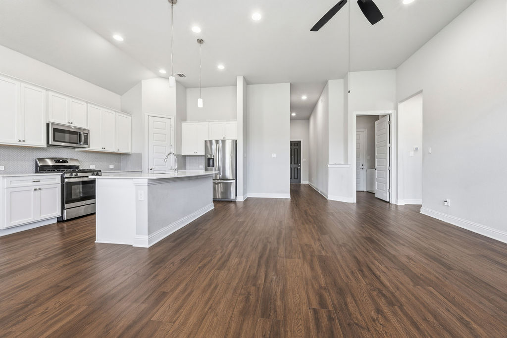 2032 Base Burner Path Leander, TX 78641 - Photo 5 of 34 Open-concept kitchen and living area featuring wood-finish flooring, white cabinetry, stainless steel appliances, and a central island with a sink and pendant lighting