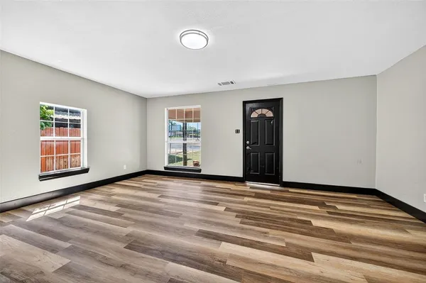 a view of an empty room with wooden floor and a window
