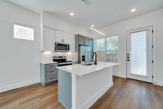 a kitchen with stainless steel appliances a stove top oven a sink a refrigerator with wooden floor and cabinets