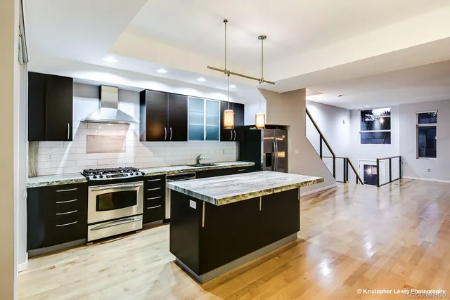 a kitchen with stainless steel appliances kitchen island granite countertop a refrigerator a stove and a sink with wooden floor